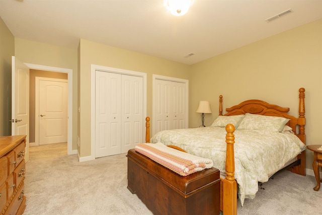 bedroom with two closets, light carpet, visible vents, and baseboards