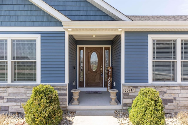 doorway to property with roof with shingles and stone siding
