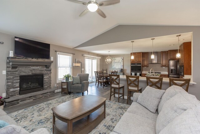 living room featuring vaulted ceiling, a stone fireplace, light wood finished floors, and a ceiling fan