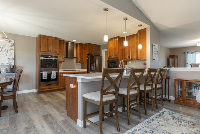 kitchen with double oven, wall chimney range hood, stovetop, a peninsula, and refrigerator with ice dispenser
