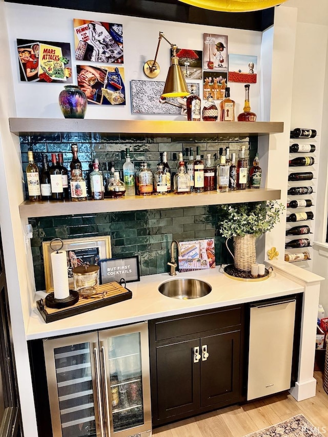 bar featuring beverage cooler, light wood-type flooring, wet bar, and a sink