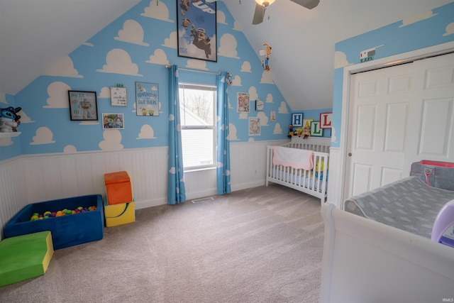 carpeted bedroom featuring a closet, wainscoting, lofted ceiling, and a nursery area
