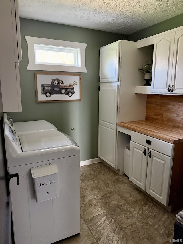 laundry room with a textured ceiling, baseboards, cabinet space, and washing machine and dryer