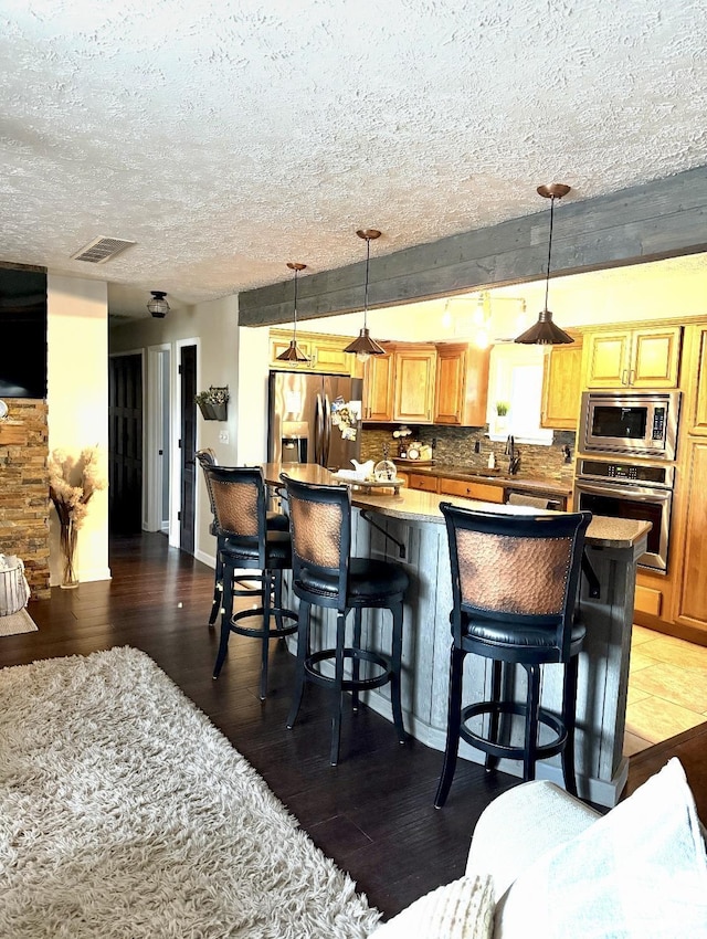 kitchen with visible vents, a kitchen island, a textured ceiling, appliances with stainless steel finishes, and wood finished floors