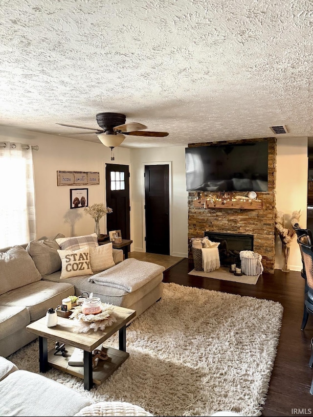 living area with a large fireplace, a ceiling fan, visible vents, a textured ceiling, and wood finished floors