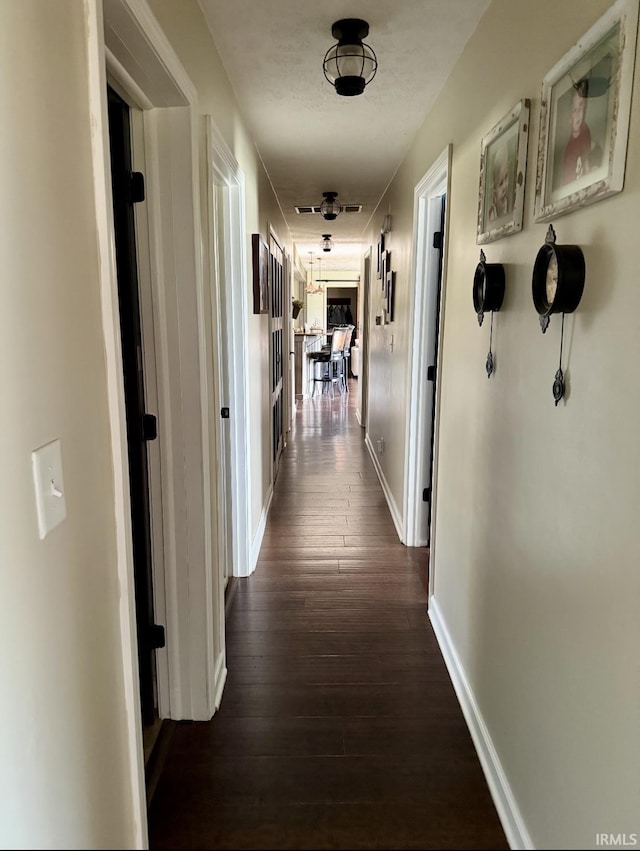 hall featuring dark wood-style flooring and baseboards