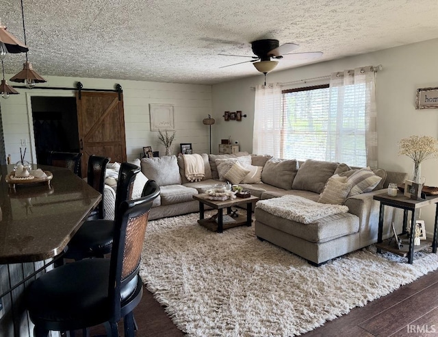living area with a ceiling fan, a textured ceiling, a barn door, and dark wood-type flooring
