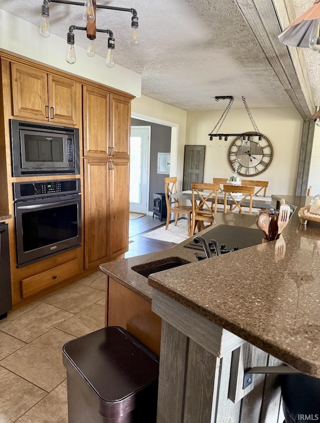 kitchen featuring dark stone counters, light tile patterned floors, brown cabinets, black microwave, and stainless steel oven