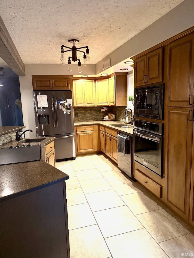 kitchen featuring decorative backsplash, light tile patterned floors, appliances with stainless steel finishes, dark countertops, and a sink