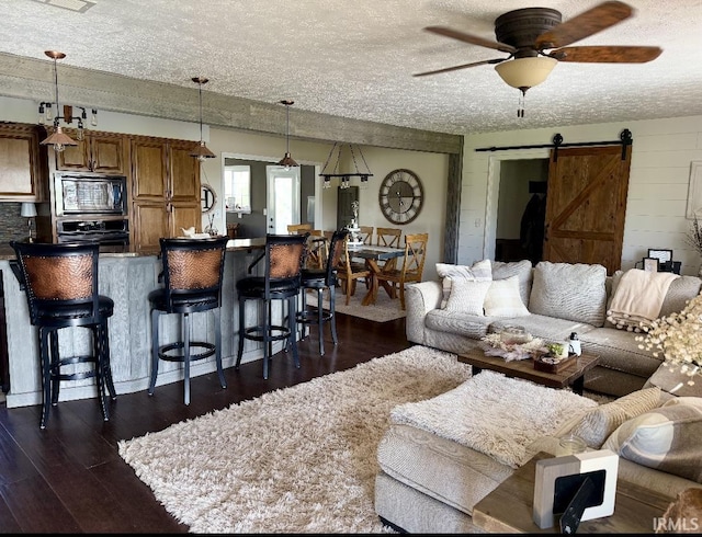 living area featuring a textured ceiling, dark wood-style flooring, ceiling fan, and a barn door