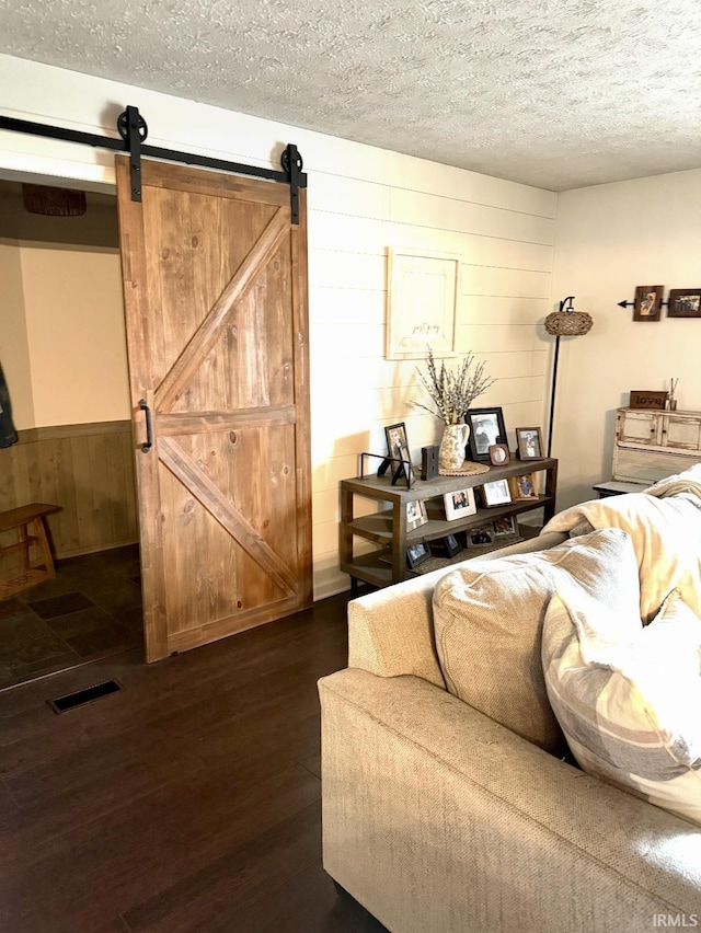 living room with wooden walls, a textured ceiling, visible vents, and a barn door