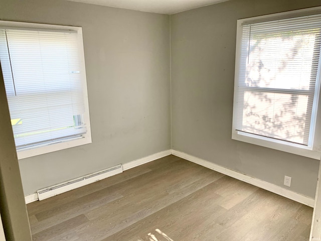 unfurnished room featuring dark wood-type flooring, baseboard heating, and plenty of natural light