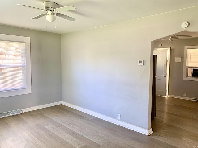 spare room with wood finished floors, visible vents, a ceiling fan, and baseboards