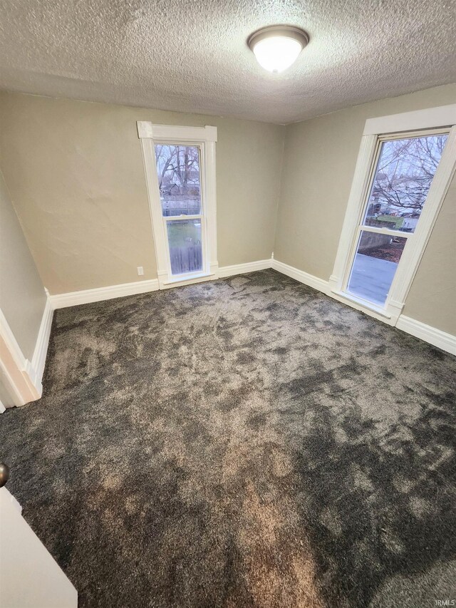 empty room with a textured ceiling, carpet flooring, and baseboards
