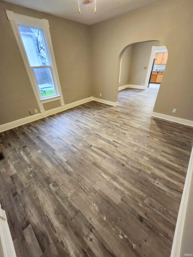 unfurnished room with arched walkways, wood finished floors, and baseboards