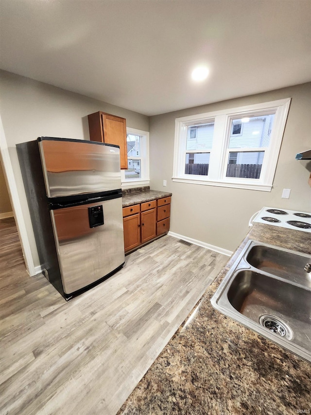 kitchen featuring brown cabinets, a sink, dark countertops, freestanding refrigerator, and light wood-type flooring