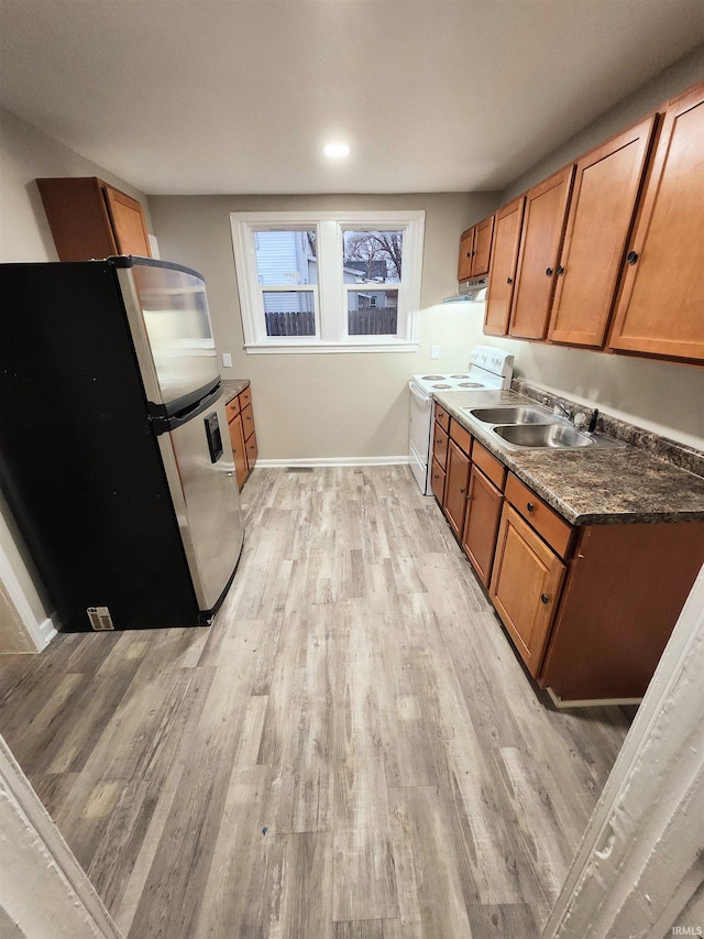 kitchen featuring brown cabinets, a sink, light wood-style floors, freestanding refrigerator, and electric range