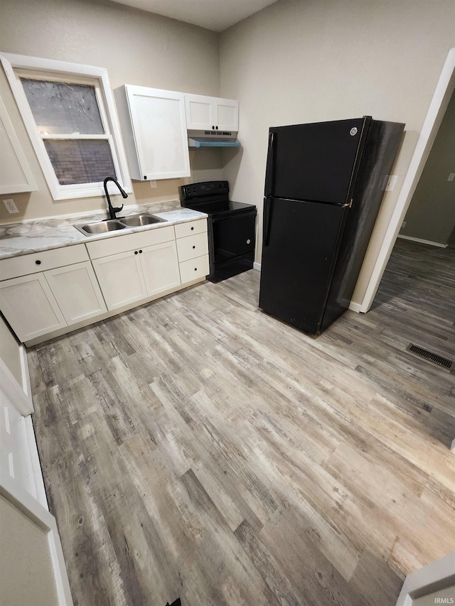kitchen featuring light wood-style flooring, a sink, visible vents, under cabinet range hood, and black appliances