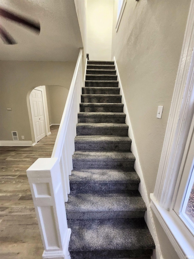 stairs with arched walkways, visible vents, wood finished floors, and baseboards