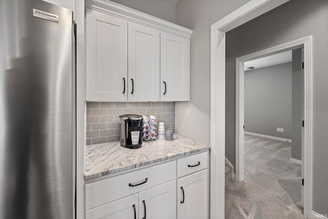 kitchen featuring white cabinetry, tasteful backsplash, light colored carpet, freestanding refrigerator, and light stone countertops