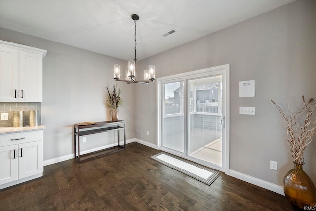 unfurnished dining area with dark wood-style floors, visible vents, a notable chandelier, and baseboards