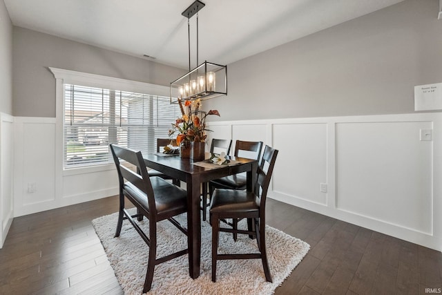 dining space featuring a wainscoted wall, an inviting chandelier, dark wood-style flooring, and a decorative wall