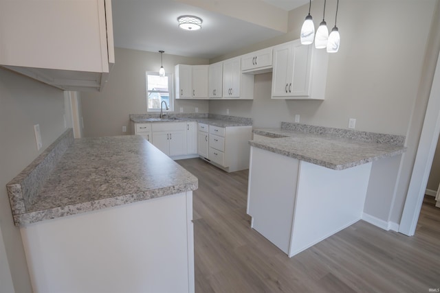 kitchen featuring white cabinets, a sink, wood finished floors, a peninsula, and hanging light fixtures