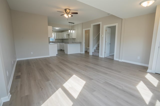 unfurnished living room with light wood-style floors, baseboards, a ceiling fan, and stairs