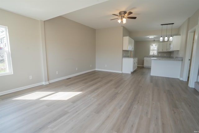 unfurnished living room with baseboards, light wood-style flooring, a ceiling fan, and a sink