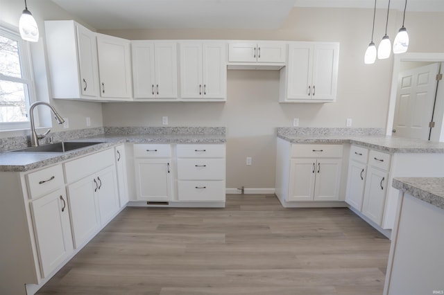 kitchen with light wood-style floors, light countertops, a sink, white cabinetry, and a peninsula