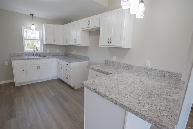 kitchen featuring pendant lighting, white cabinetry, a sink, light wood-type flooring, and a peninsula