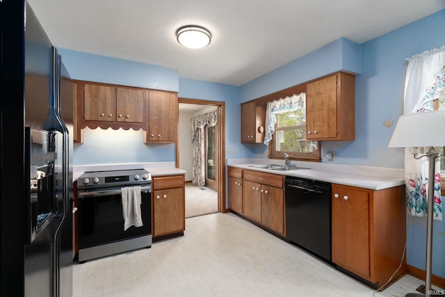 kitchen featuring light floors, brown cabinetry, light countertops, black appliances, and a sink