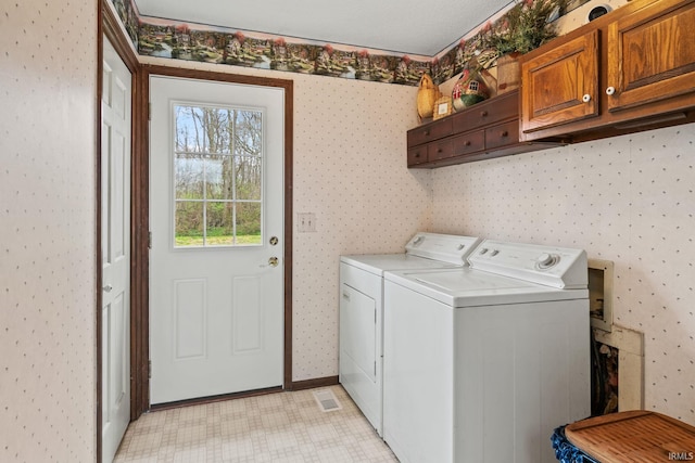 washroom featuring washing machine and dryer, visible vents, wallpapered walls, baseboards, and cabinet space