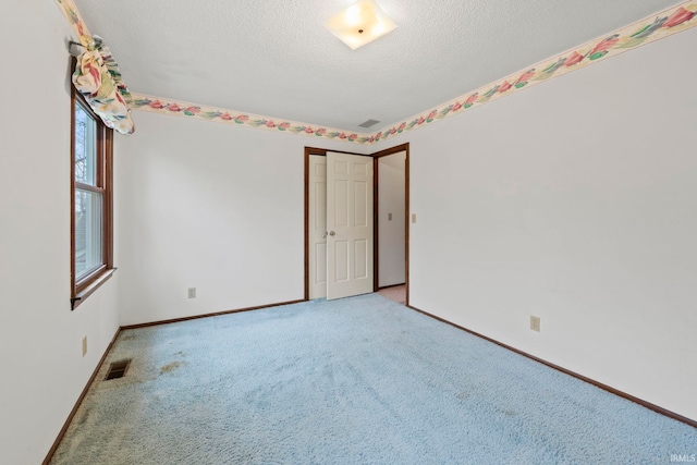 empty room with a textured ceiling, visible vents, baseboards, and light carpet