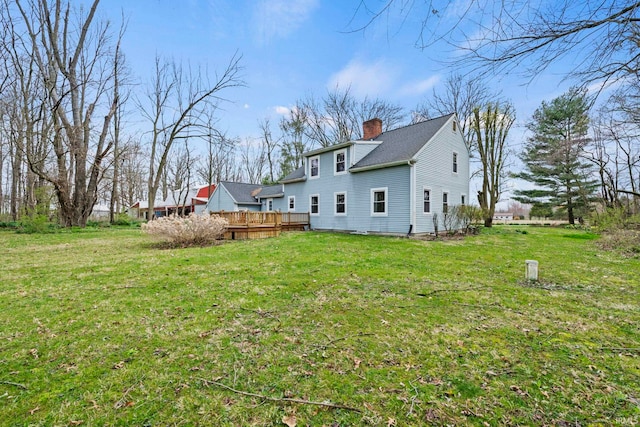rear view of property featuring a chimney, a wooden deck, and a lawn