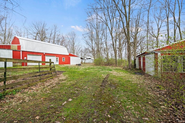 view of yard with a garage, an outdoor structure, dirt driveway, a pole building, and fence