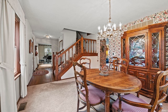carpeted dining room with visible vents, an inviting chandelier, and stairs