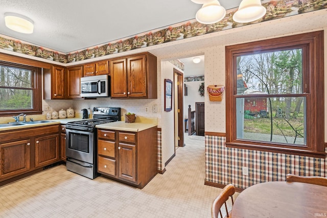 kitchen with stainless steel appliances, light countertops, wallpapered walls, and a sink