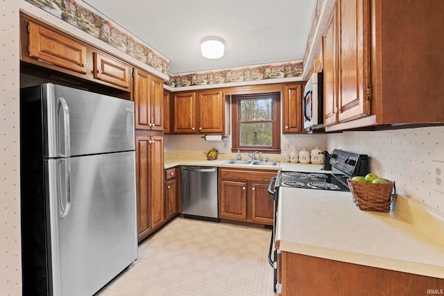 kitchen featuring wallpapered walls, appliances with stainless steel finishes, light countertops, brown cabinets, and a sink