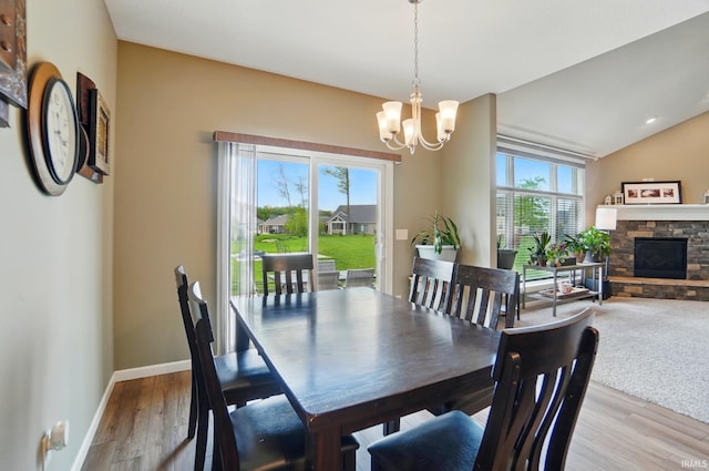 dining room featuring a chandelier, light wood-type flooring, a fireplace, baseboards, and lofted ceiling