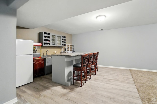 kitchen with freestanding refrigerator, a breakfast bar, a sink, light wood-style flooring, and baseboards