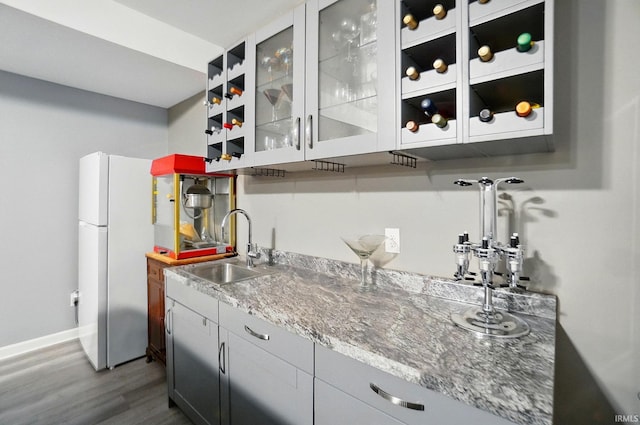 indoor wet bar with dark wood-type flooring, freestanding refrigerator, and baseboards