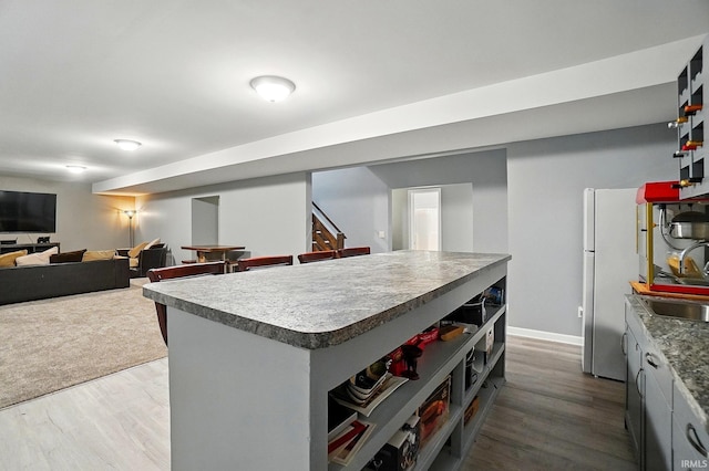 kitchen featuring wood finished floors, a sink, a kitchen island, and freestanding refrigerator