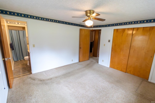 unfurnished bedroom featuring a textured ceiling, connected bathroom, carpet flooring, ceiling fan, and a closet