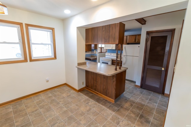 kitchen with brown cabinets, light countertops, baseboards, white appliances, and a peninsula