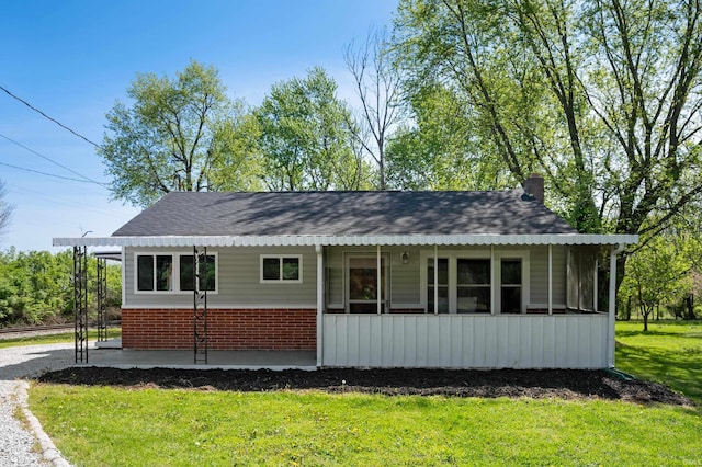 manufactured / mobile home with a chimney, brick siding, a front yard, and roof with shingles