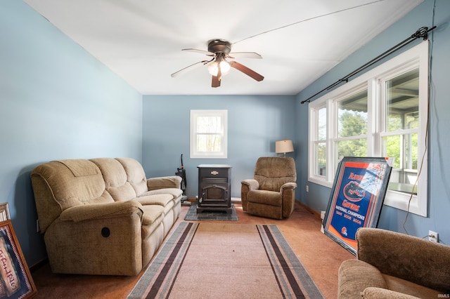 living area with a wealth of natural light, a wood stove, ceiling fan, and light colored carpet