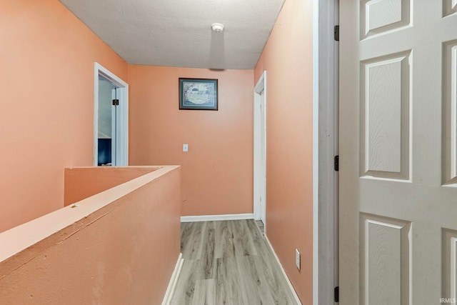 hall featuring baseboards, light wood-style floors, a textured ceiling, and an upstairs landing