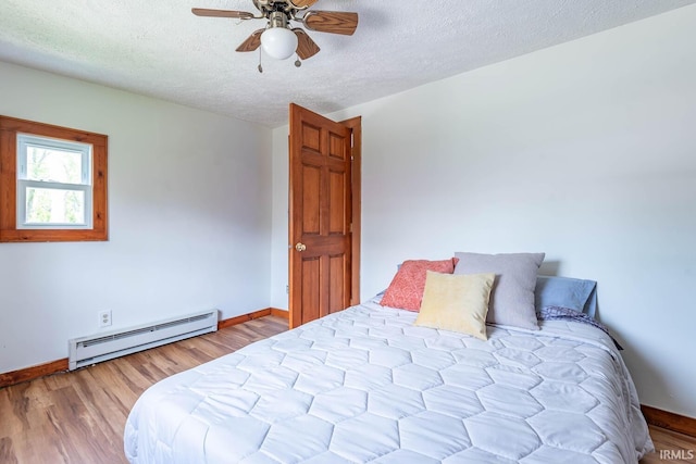 bedroom with a baseboard heating unit, wood finished floors, baseboards, and a textured ceiling