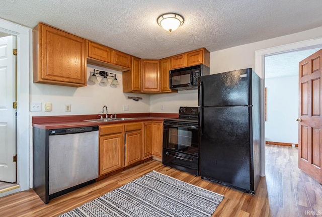kitchen featuring black appliances, a sink, light wood finished floors, dark countertops, and a textured ceiling
